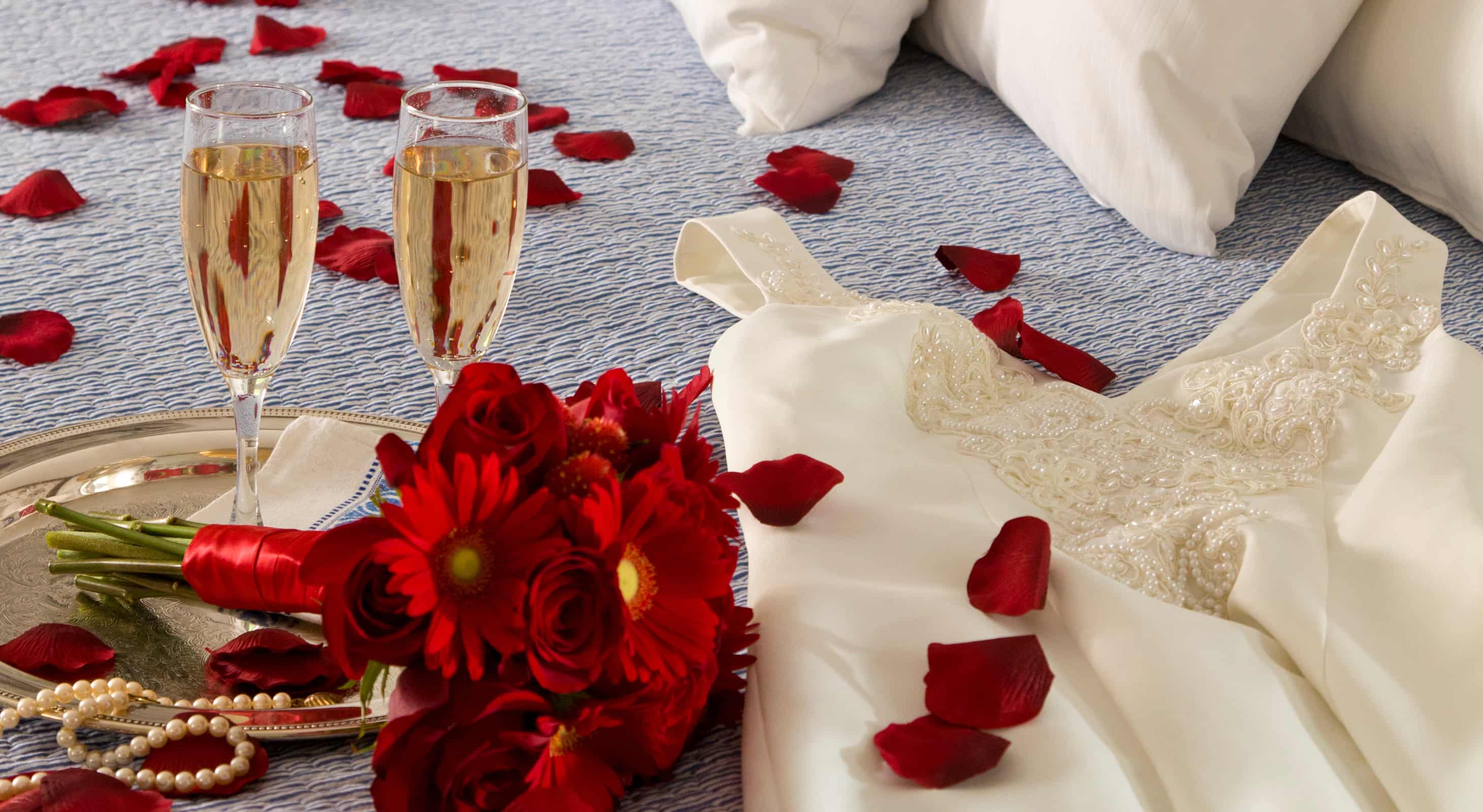 Champagne, flowers and wedding dress on bed